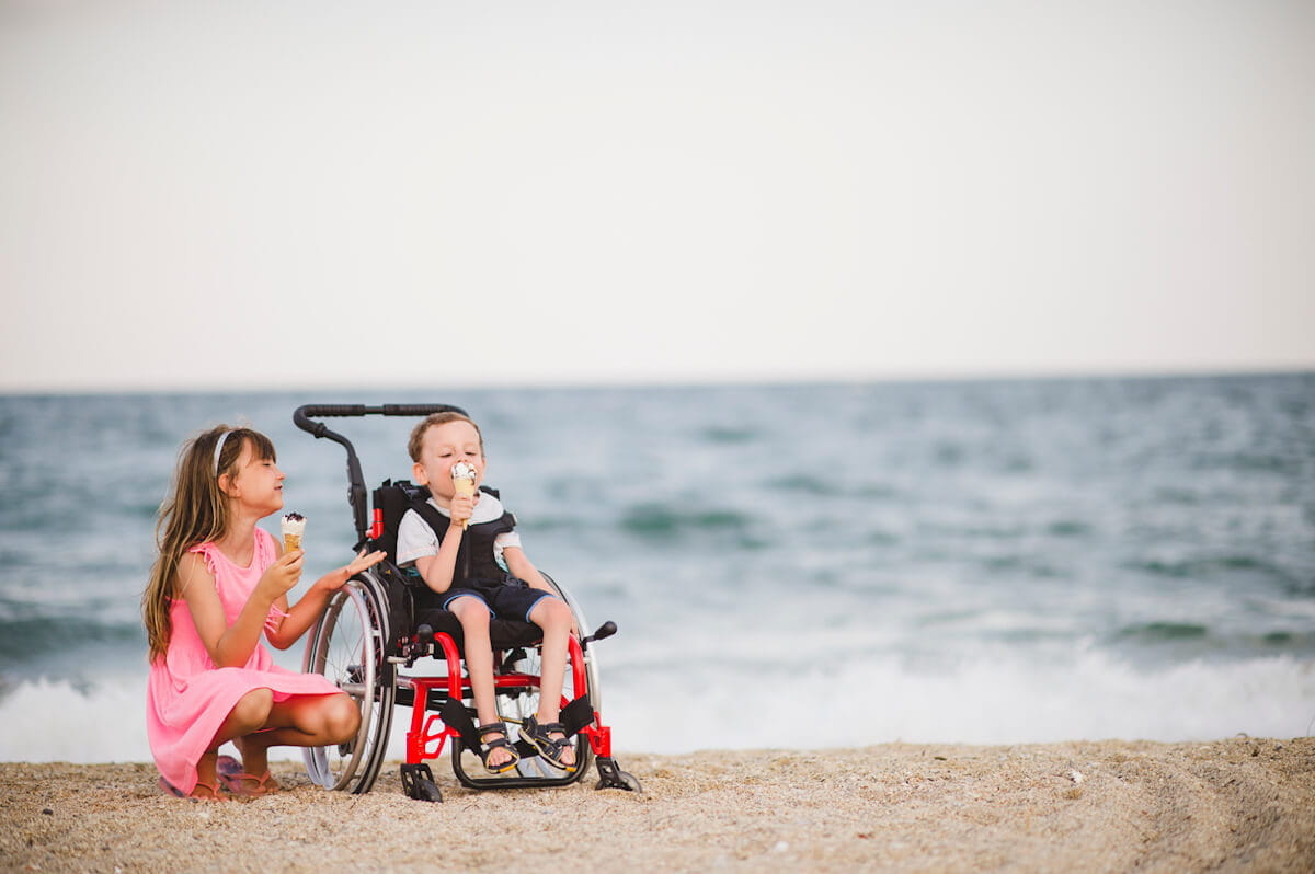 Children eating ice cream on a beach, with one child sitting in a wheelchair