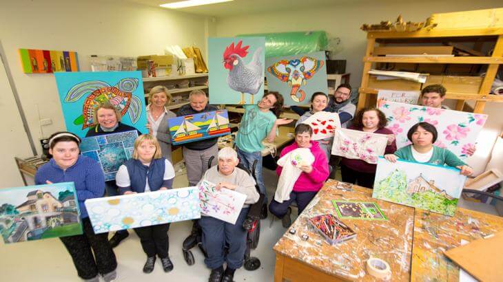 Group of artists from QArt holding up their paintings and artworks