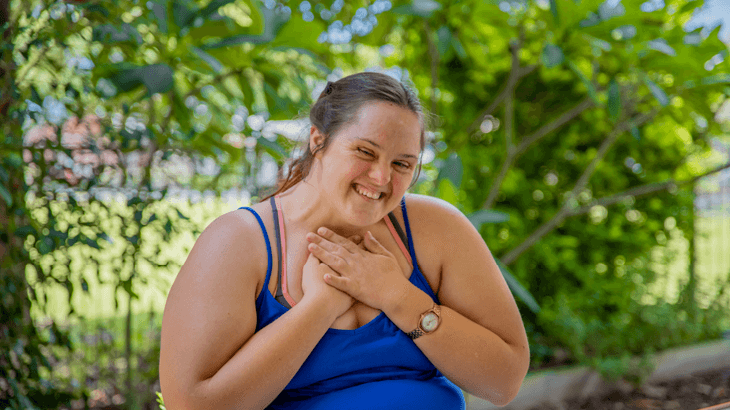 Person smiling with arms in heartfelt pose