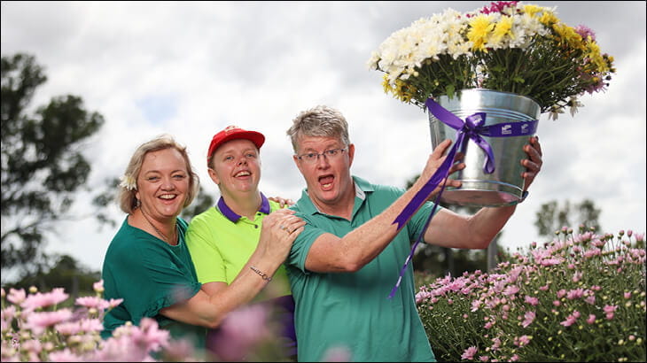 Smiling ladies holding up a large bucket of flowers