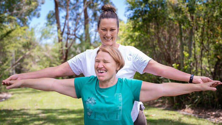 Smiling support worker and client stand with arms out