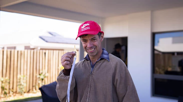 Smiling man holding up a key in front of a home